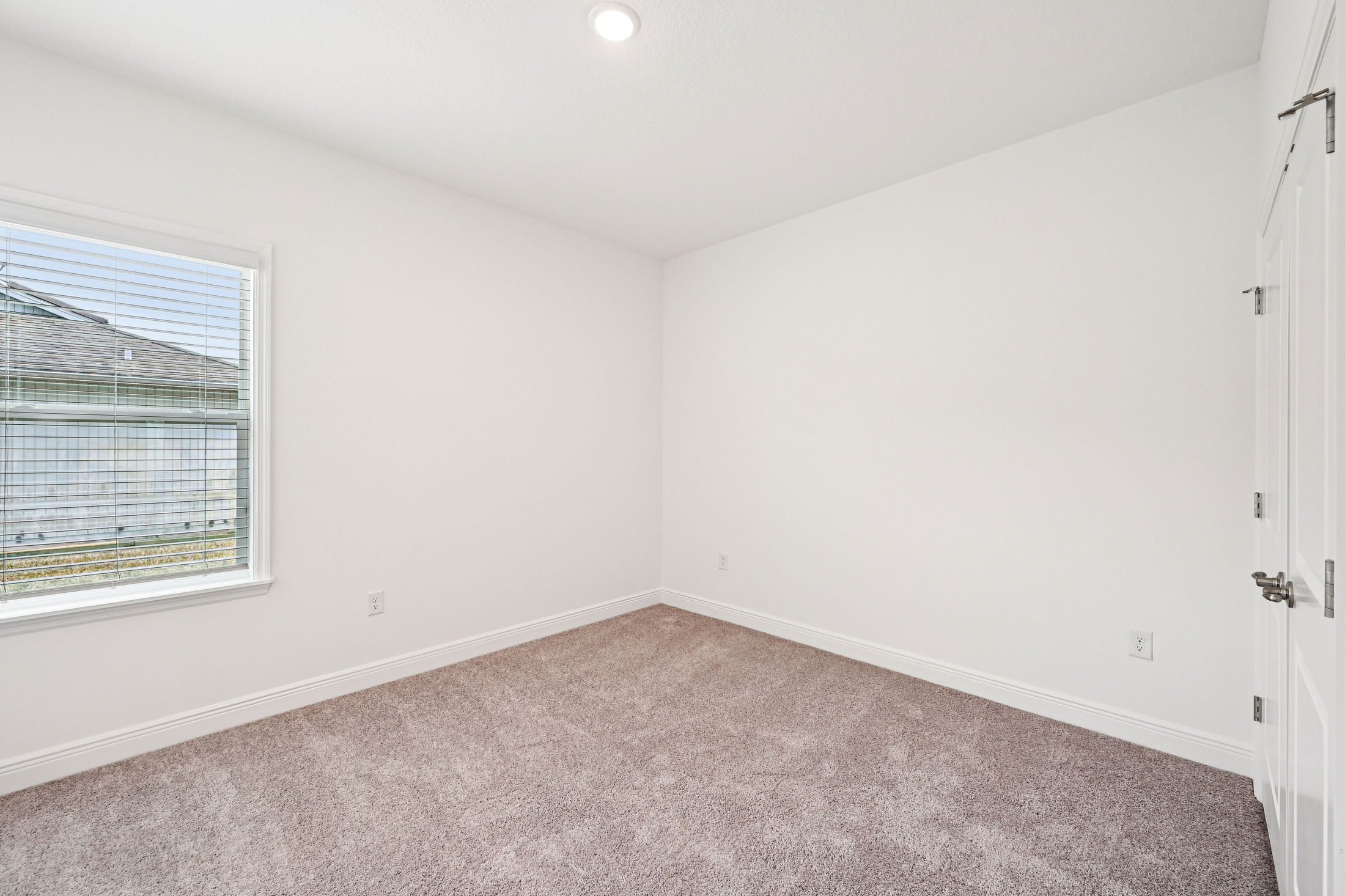 Bright and empty bedroom with plush carpet and a large window showcasing natural light.