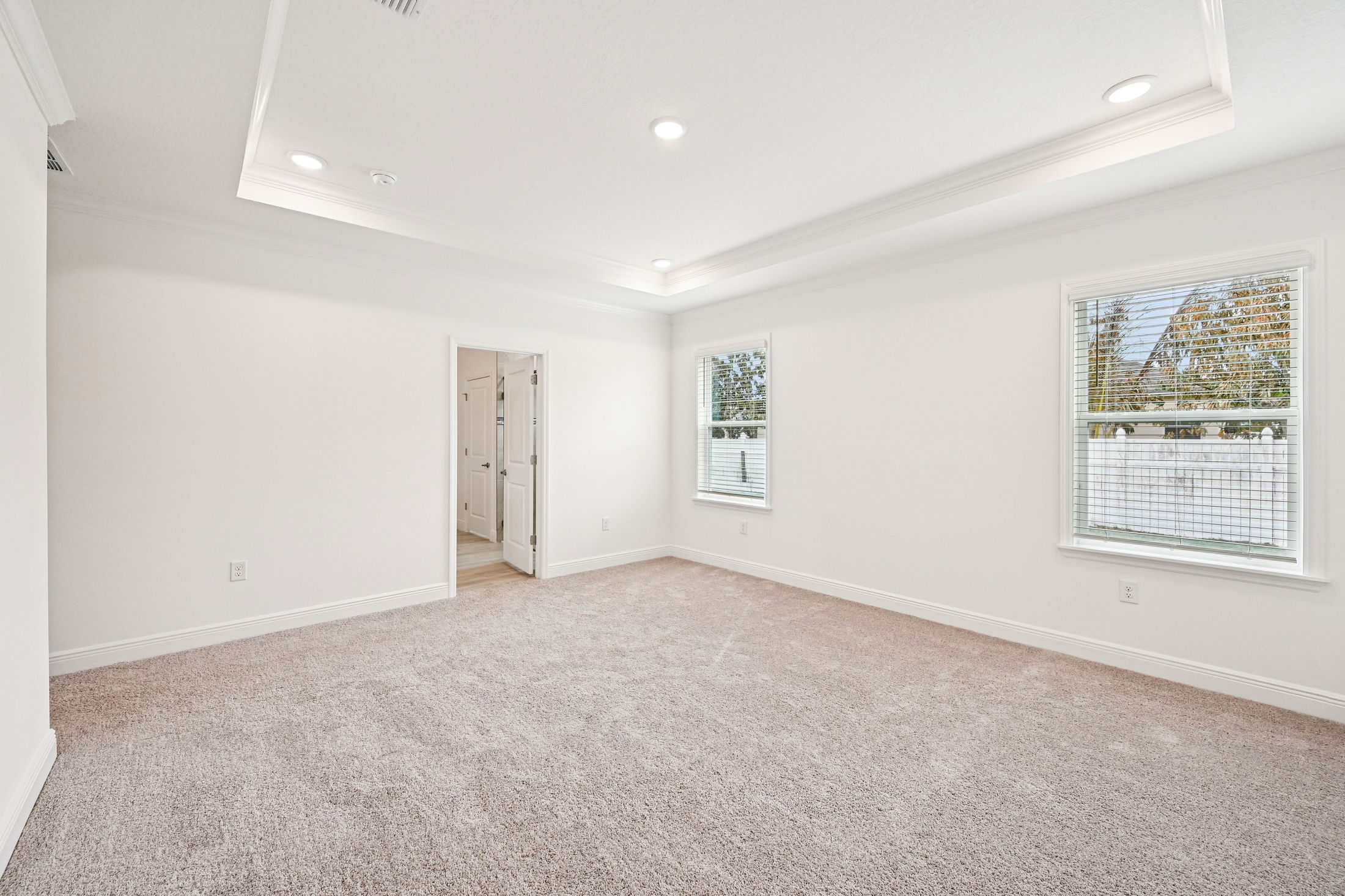 Spacious and bright empty bedroom with soft carpet flooring and large windows overlooking a fenced yard.
