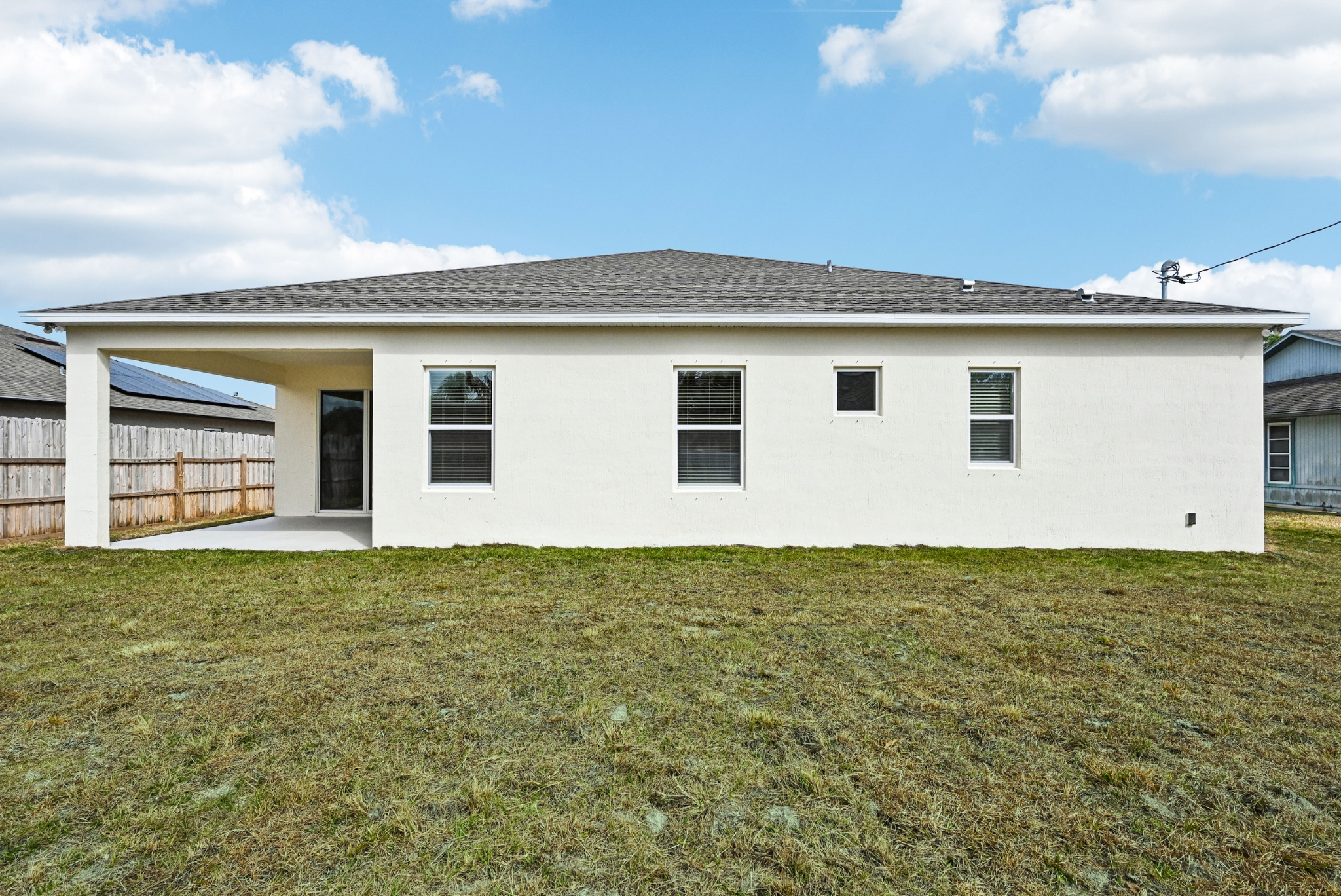 A modern, single-story home with a clean white exterior, large windows, and a spacious backyard under a blue sky.