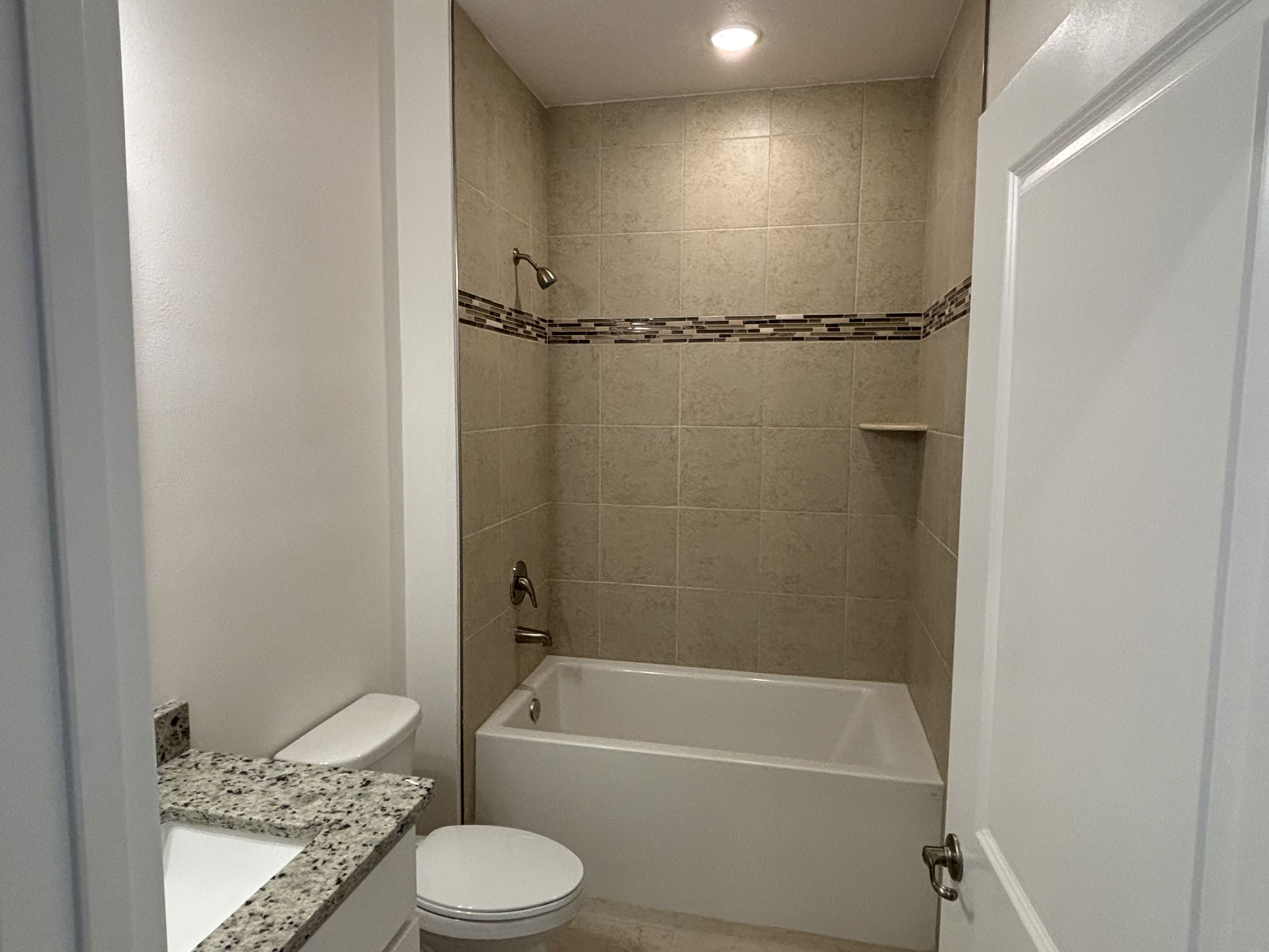 Modern bathroom featuring a tiled shower-bathtub combination, granite countertop, and recessed lighting.