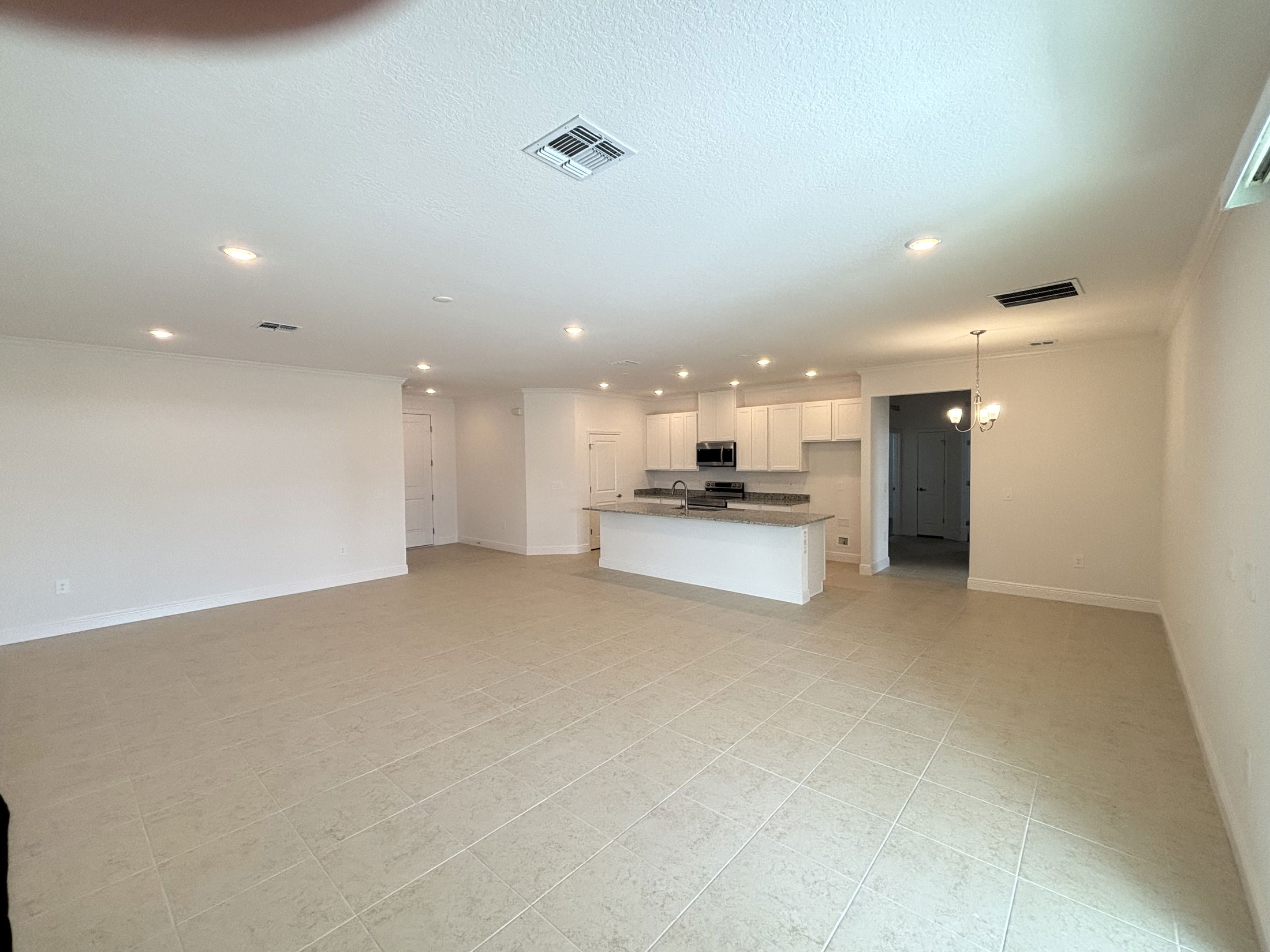 Spacious open-concept kitchen and living area with tiled floors, recessed lighting, and modern appliances in a newly constructed home.