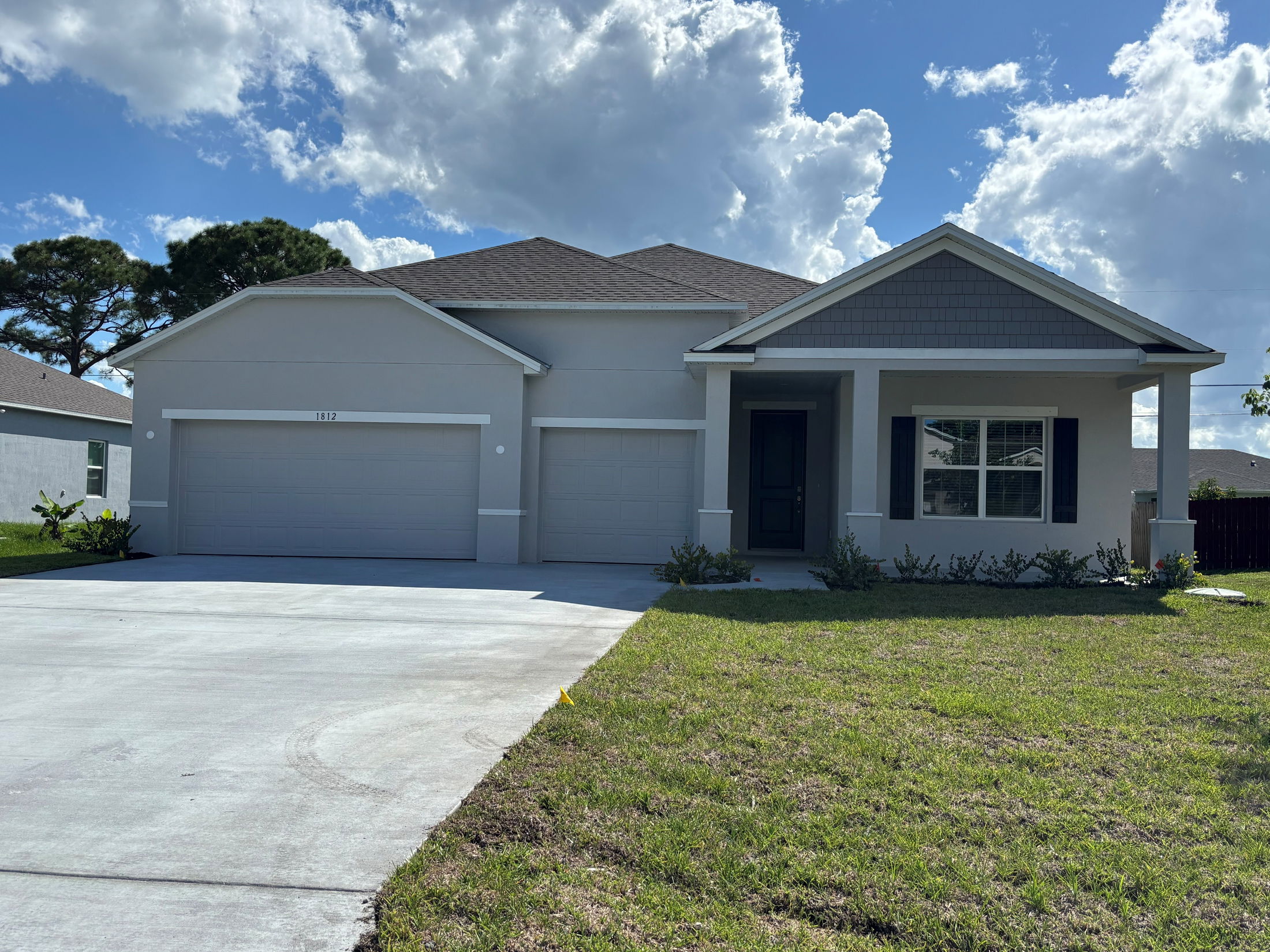 Modern single-story home with a three-car garage and a well-maintained front lawn under a partly cloudy sky.