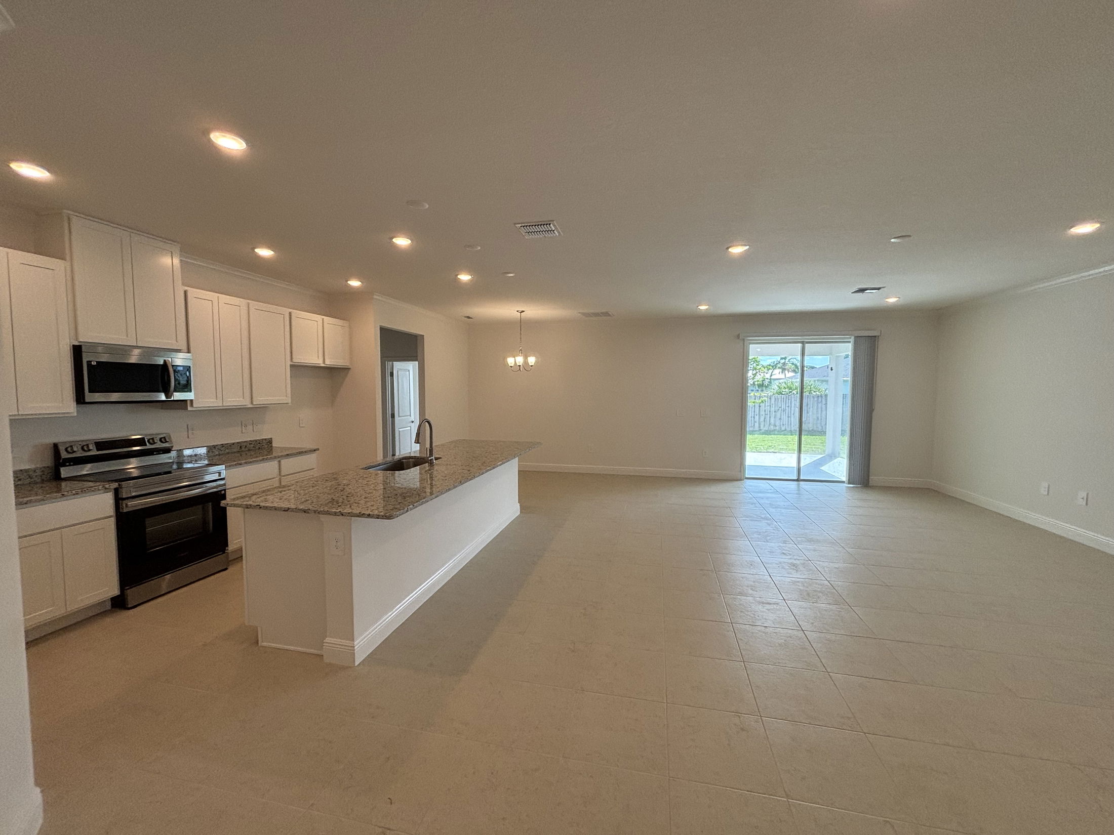 Spacious modern kitchen and open living area with tile flooring, granite countertops, and sliding glass doors to a backyard.