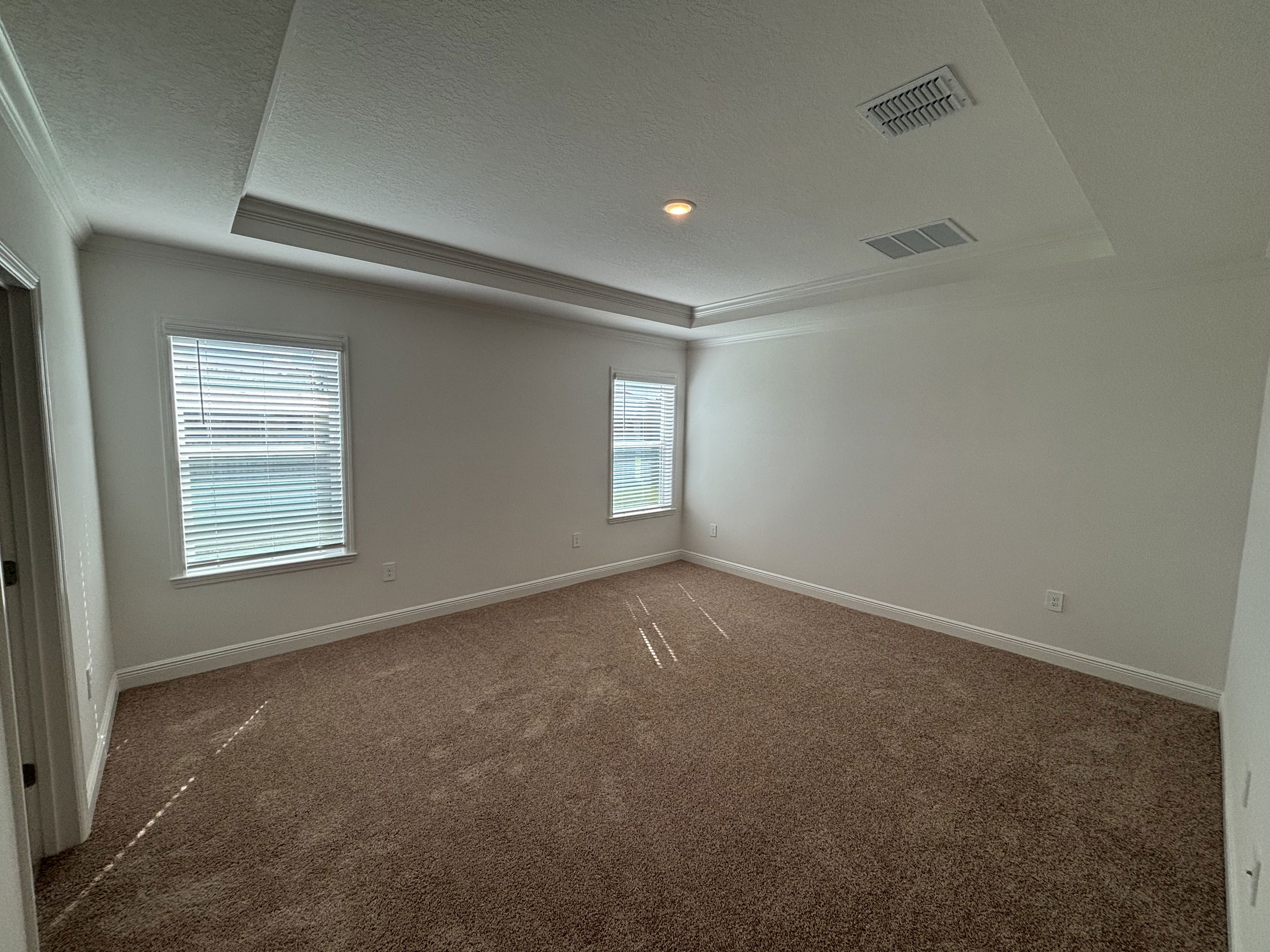 Empty room with brown carpet, white walls, two large windows, and a tray ceiling with recessed lighting.