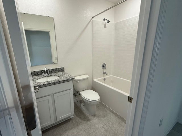 Modern white bathroom featuring a bathtub, granite countertop sink, and tiled floor.