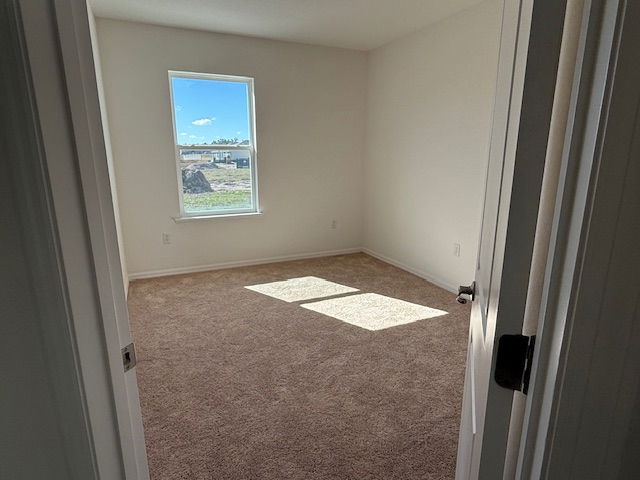 Empty, sunlit room with beige carpet and a window overlooking a construction site.