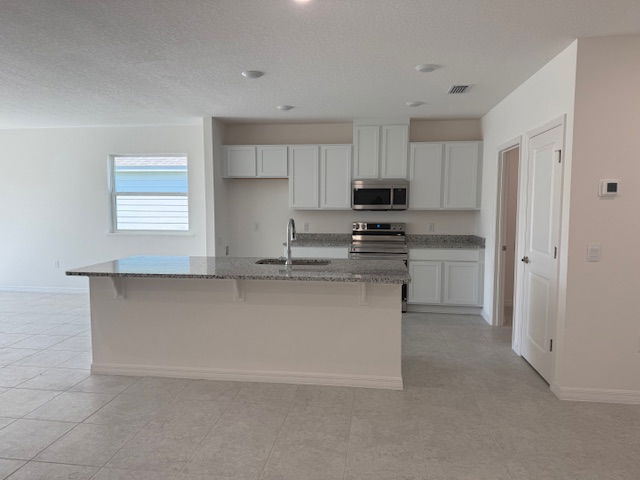 Modern kitchen with white cabinets, granite countertops, and stainless steel appliances in an open-concept layout.