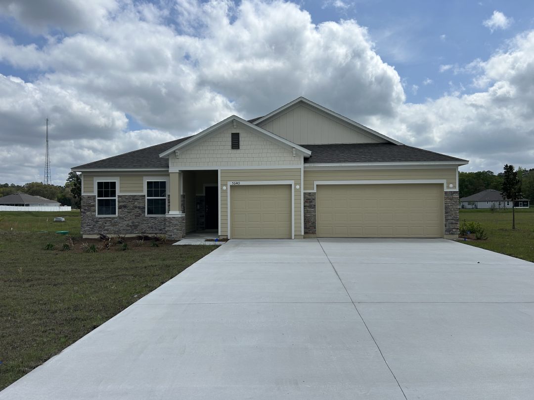 Modern single-story home with stone and siding exterior, featuring a large three-car garage and a spacious driveway under a partly cloudy sky.