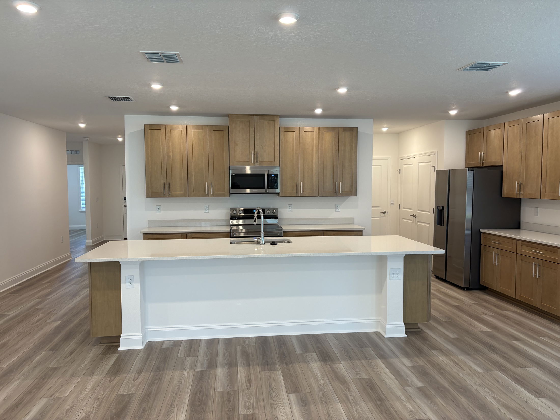 Modern kitchen interior with wooden cabinets, stainless steel appliances, and a spacious island countertop featuring hardwood flooring.
