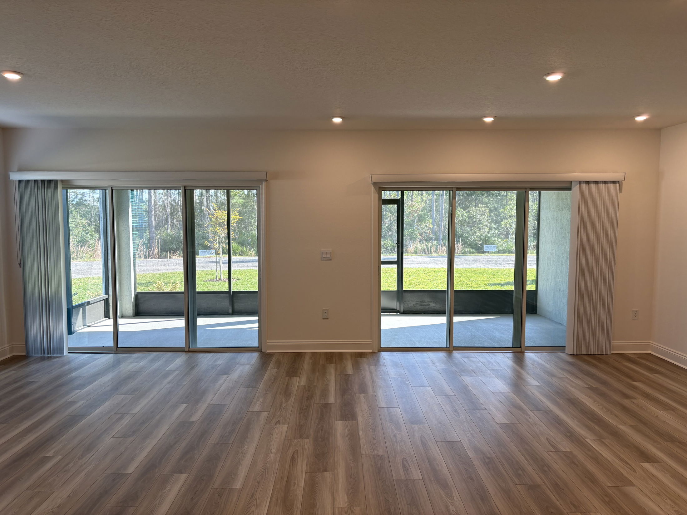 Bright and airy living room with sliding glass doors and a view of a landscaped backyard featuring large windows and wooden flooring.