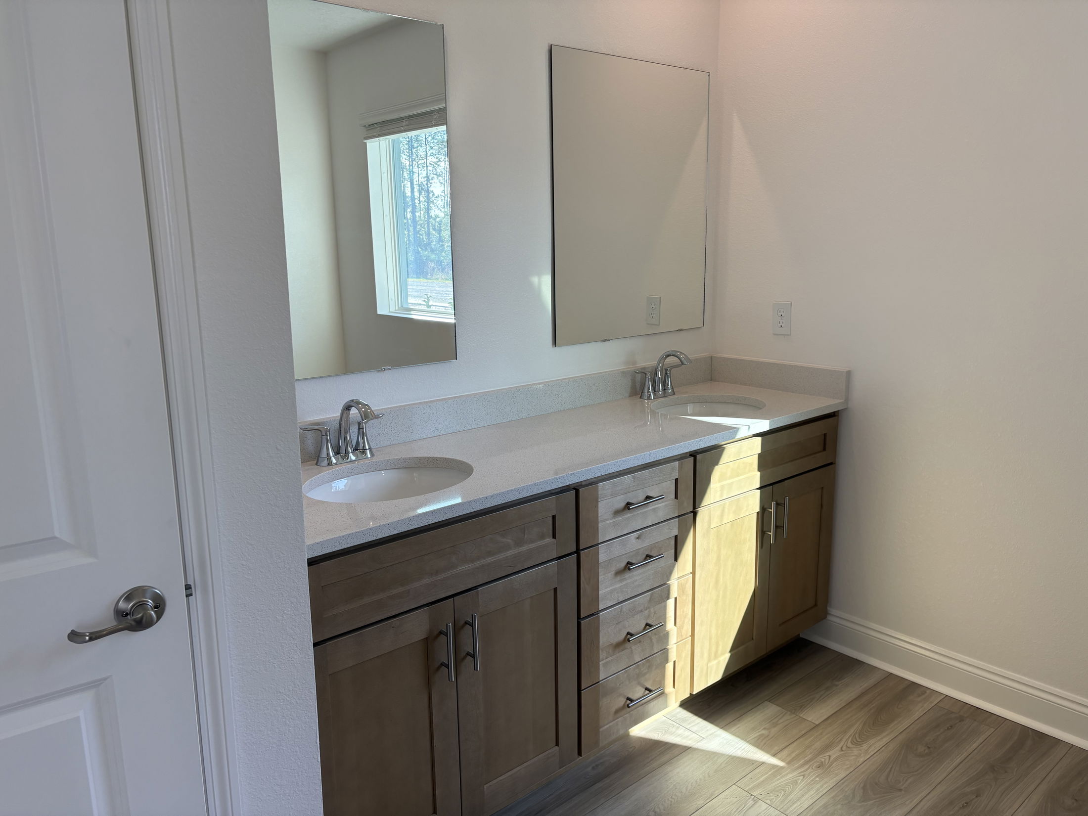 Bright and modern bathroom featuring dual sinks, wooden cabinetry, and ample natural light from a nearby window.