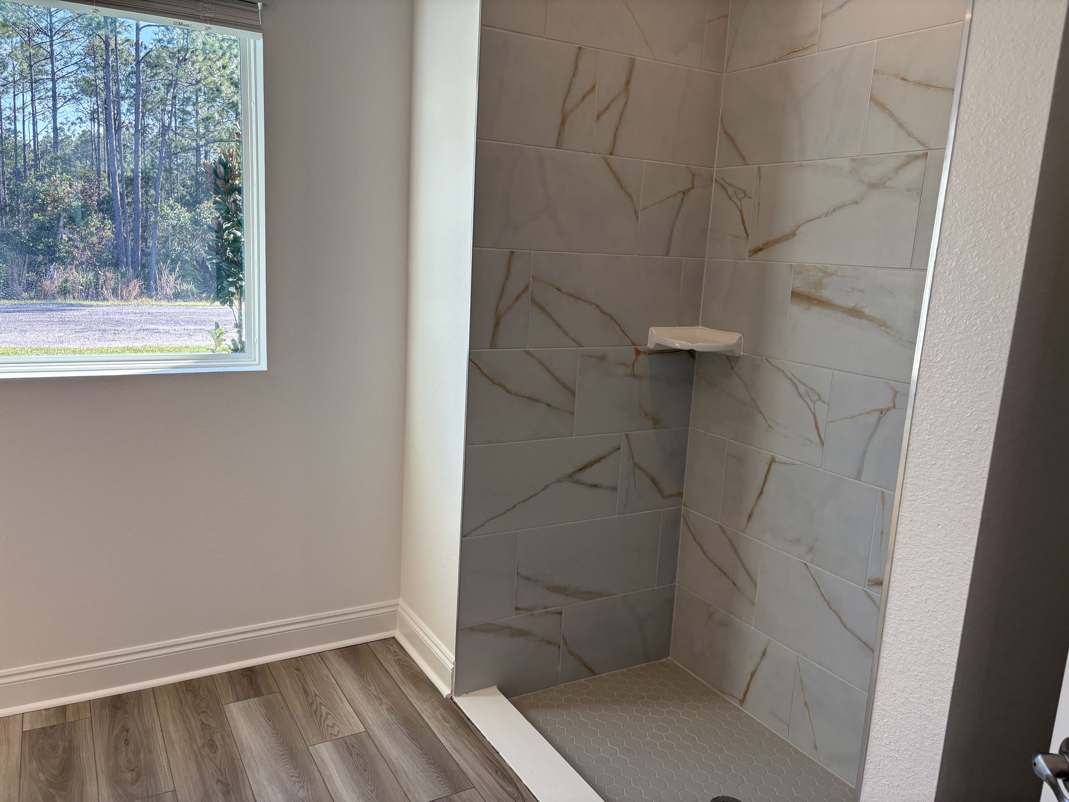Modern bathroom shower featuring elegant gray tiles with gold veining and a window displaying a natural outdoor view.