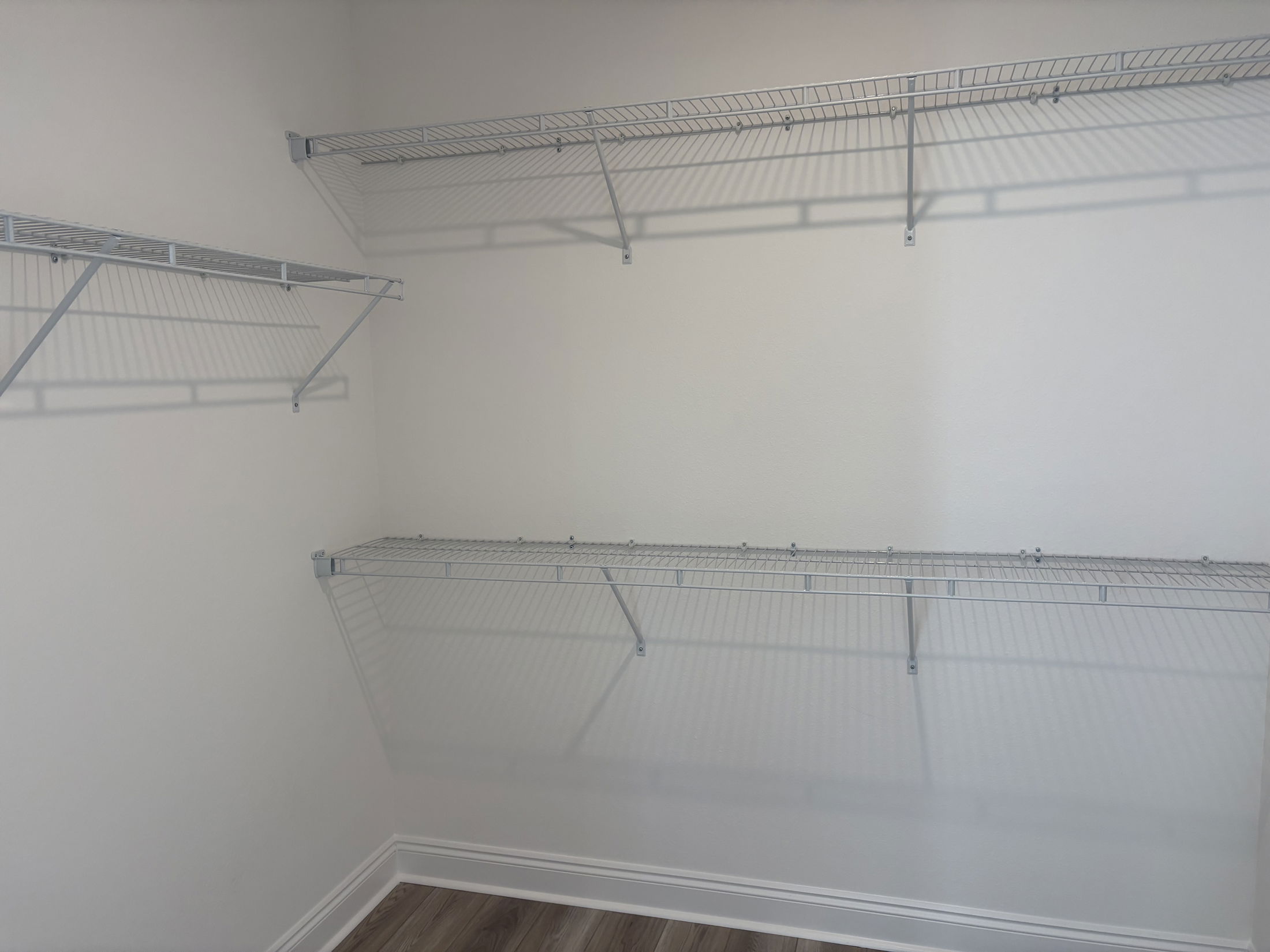 Empty closet with metal wire shelving installed on the walls, featuring shadows cast on a light-colored wall.