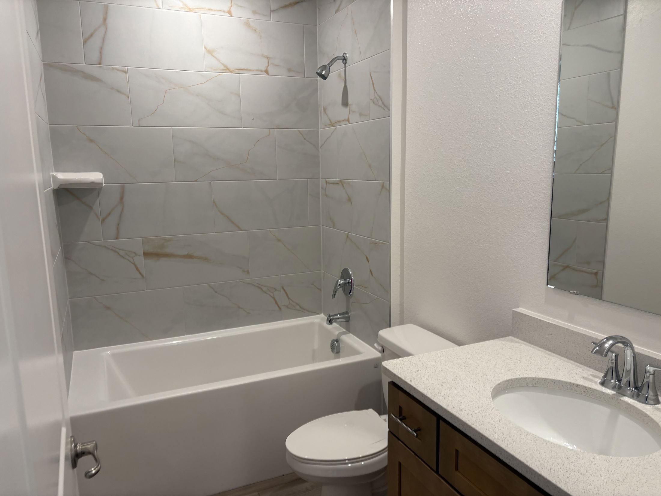 Modern bathroom design featuring a white bathtub, marble-patterned tile walls, a sleek vanity with a sink, and a minimalist mirror.