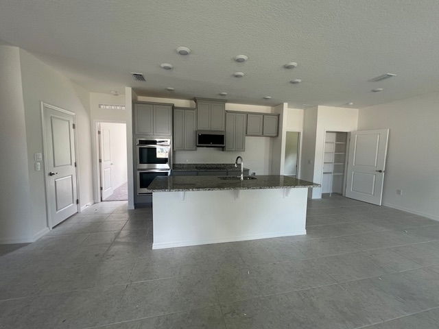 Modern kitchen with gray cabinets, island, and stainless steel appliances in a spacious open floor plan.