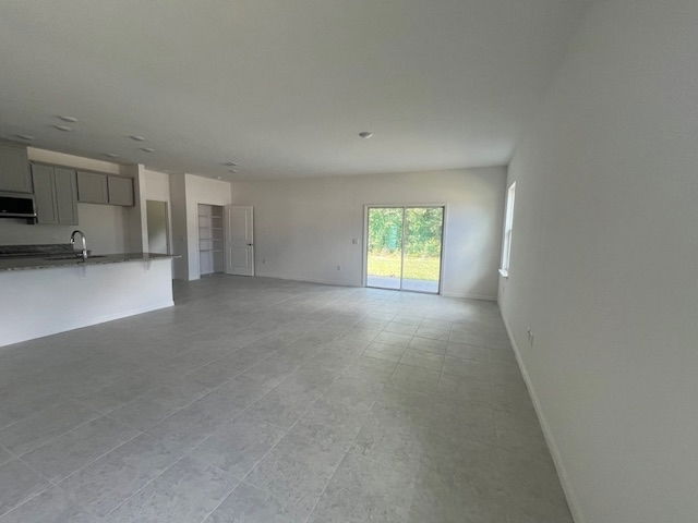 Spacious open-concept living area with tiled flooring, modern kitchen, and large windows leading to a patio.
