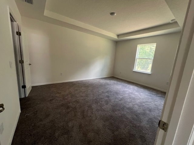 Spacious empty bedroom with beige walls, tray ceiling, and carpet flooring, featuring a single window showing natural light.