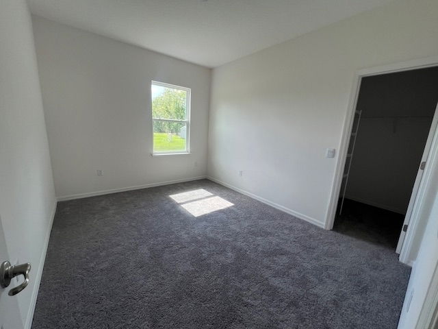 Empty bedroom with gray carpet, white walls, a single window providing natural light, and a doorway leading to a closet.