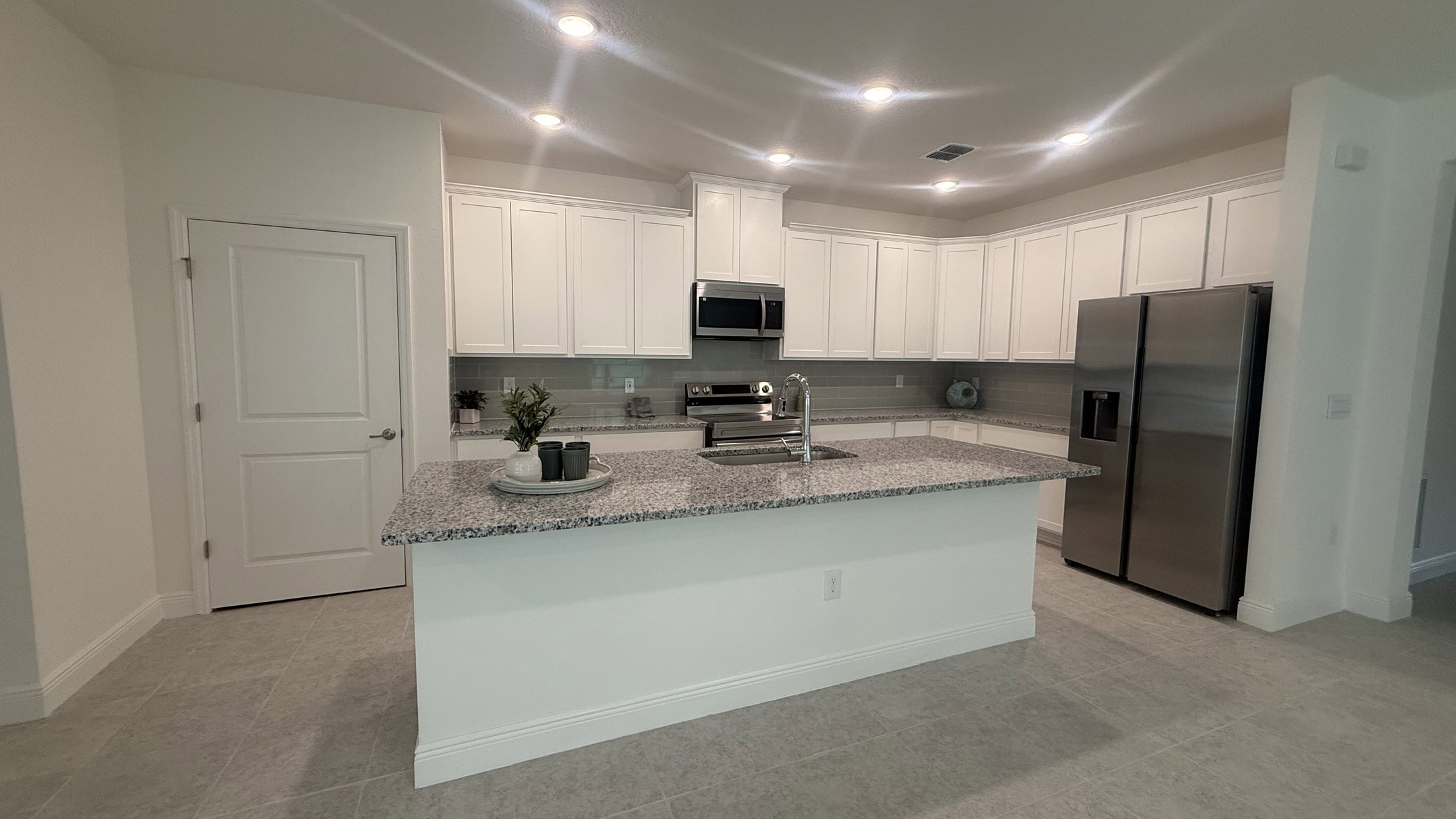 Modern kitchen with white cabinetry, stainless steel appliances, and a large granite island.