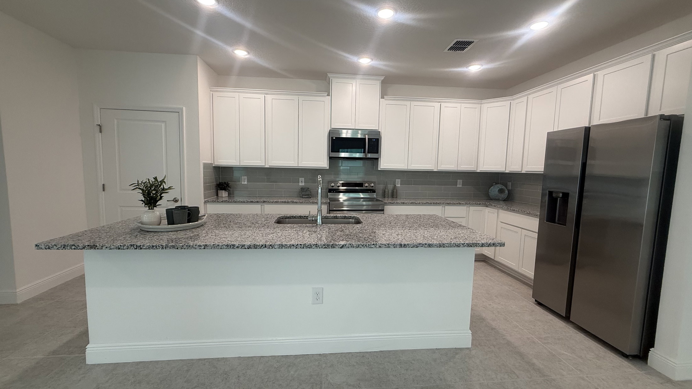 Modern kitchen featuring white cabinets, stainless steel appliances, and a spacious granite countertop island.