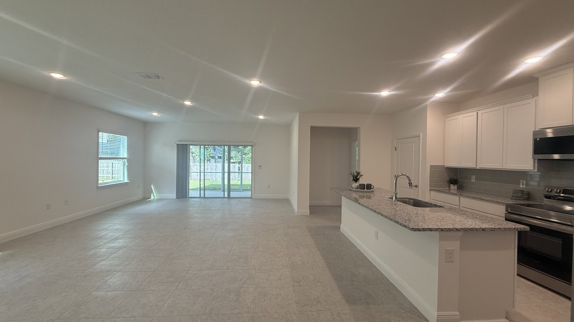 Spacious open-concept living area with a kitchen featuring a granite countertop and stainless steel appliances, large windows, and sliding glass doors leading to an outdoor space.