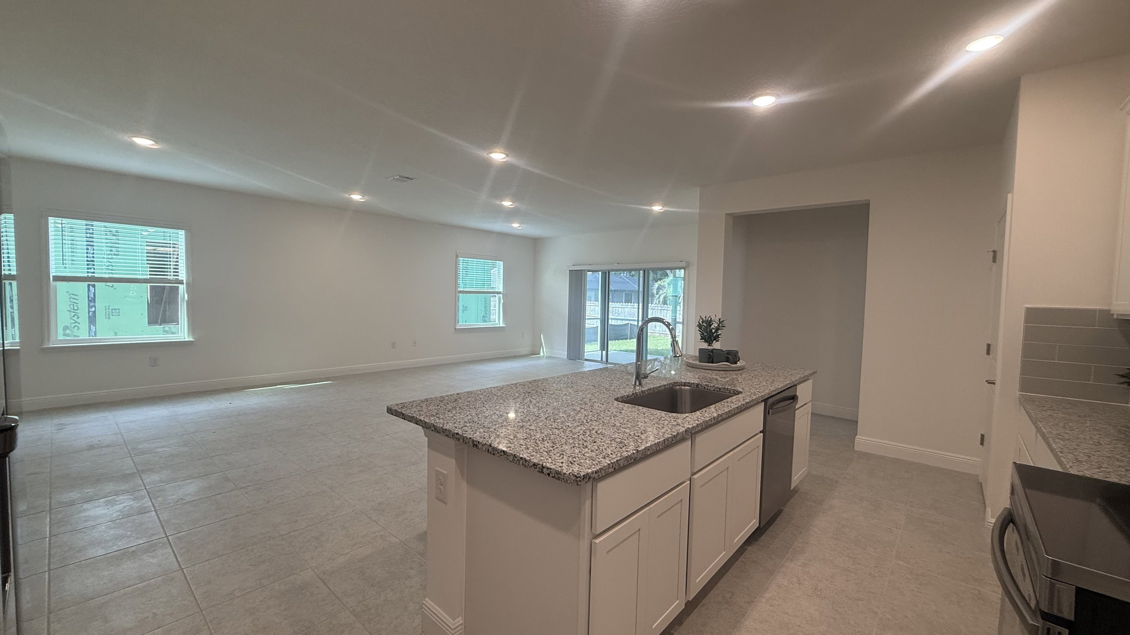 Spacious interior view of a modern kitchen and living area featuring granite countertops and large windows.