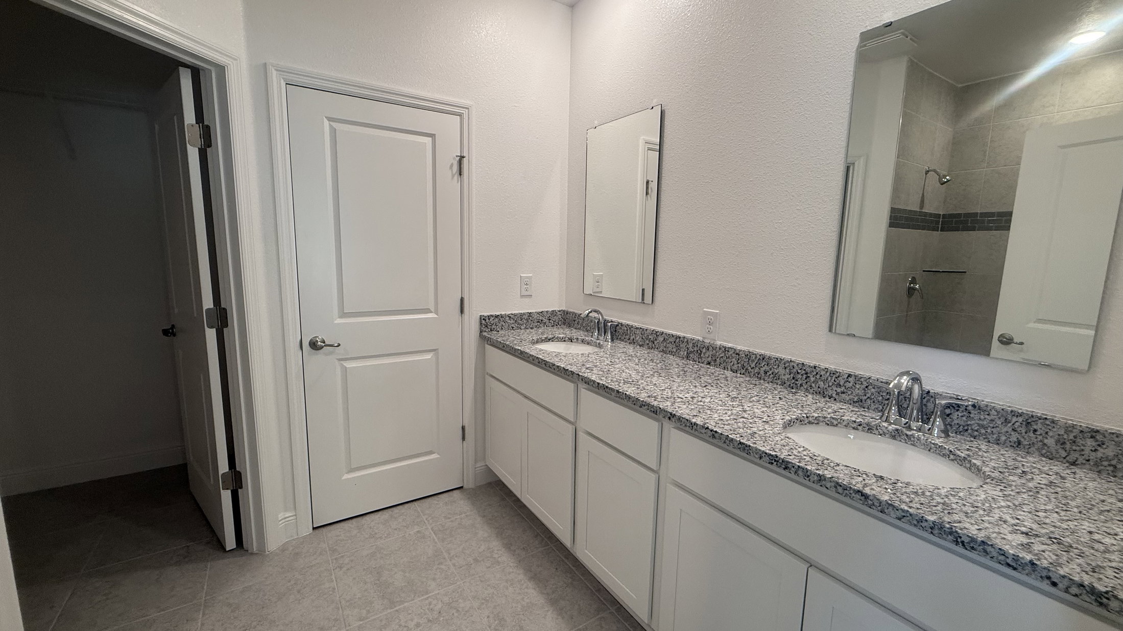 Modern bathroom featuring dual sinks, granite countertop, and a walk-in shower.