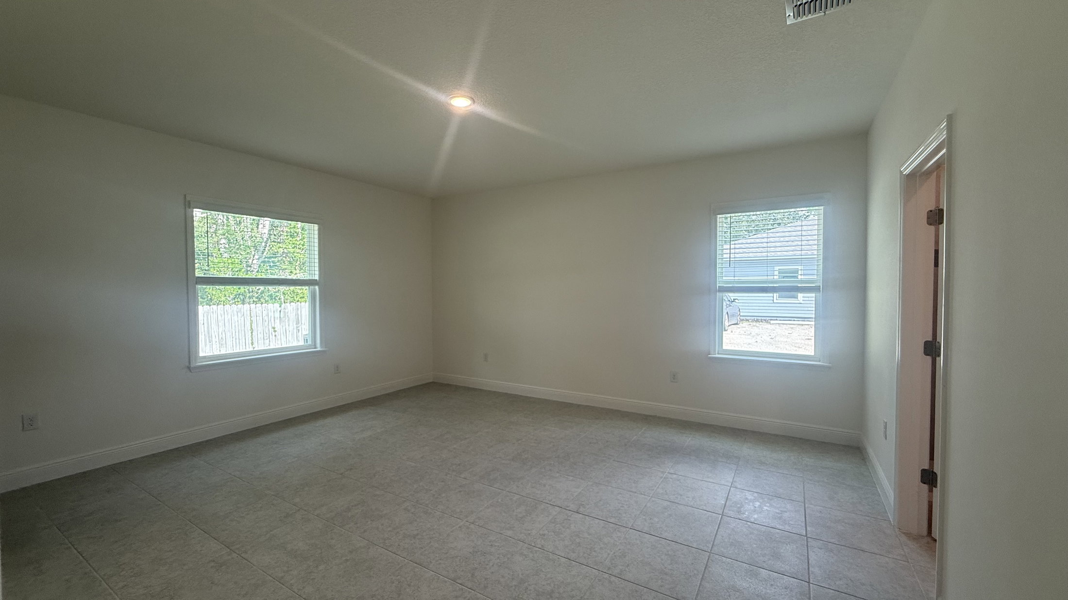 A bright, empty room with two windows and light-colored walls and flooring.