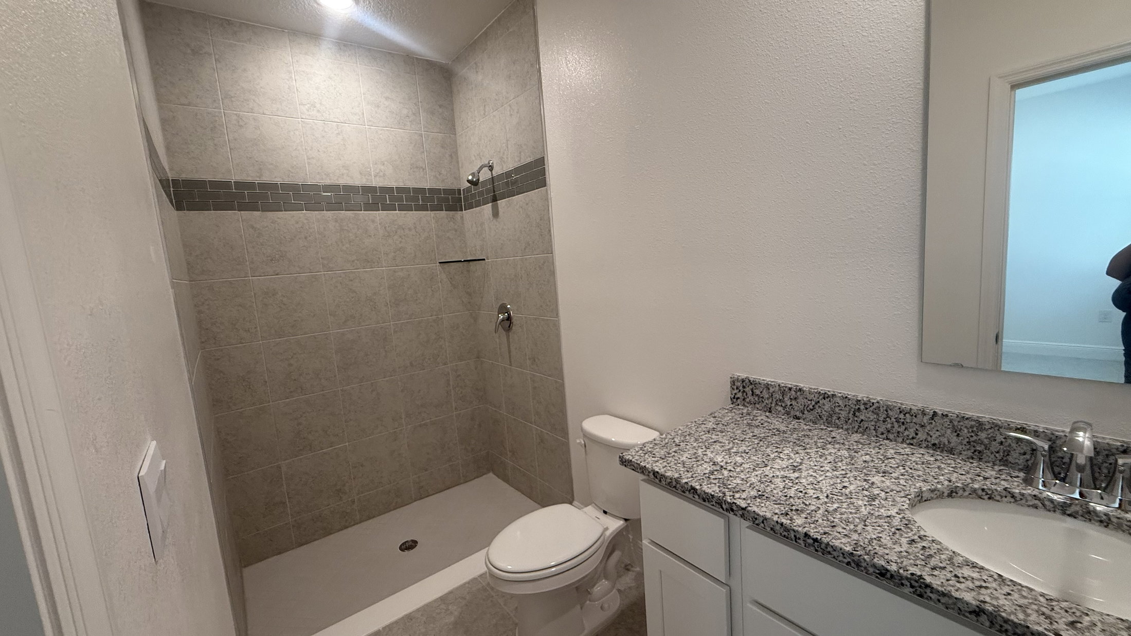 A modern bathroom featuring a walk-in shower, a toilet, and a granite countertop with a sink.