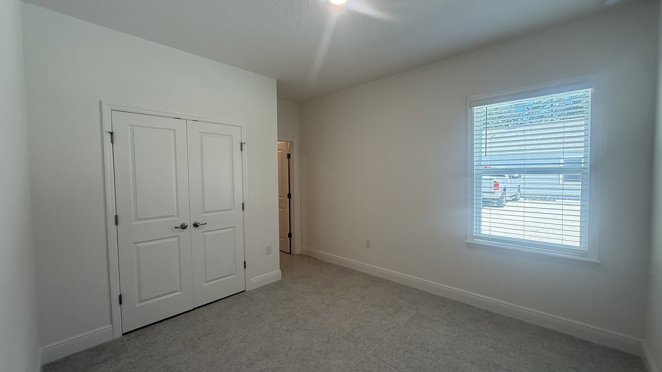 A bright, empty room with light-colored walls, tiled floor, and a closed double door closet.
