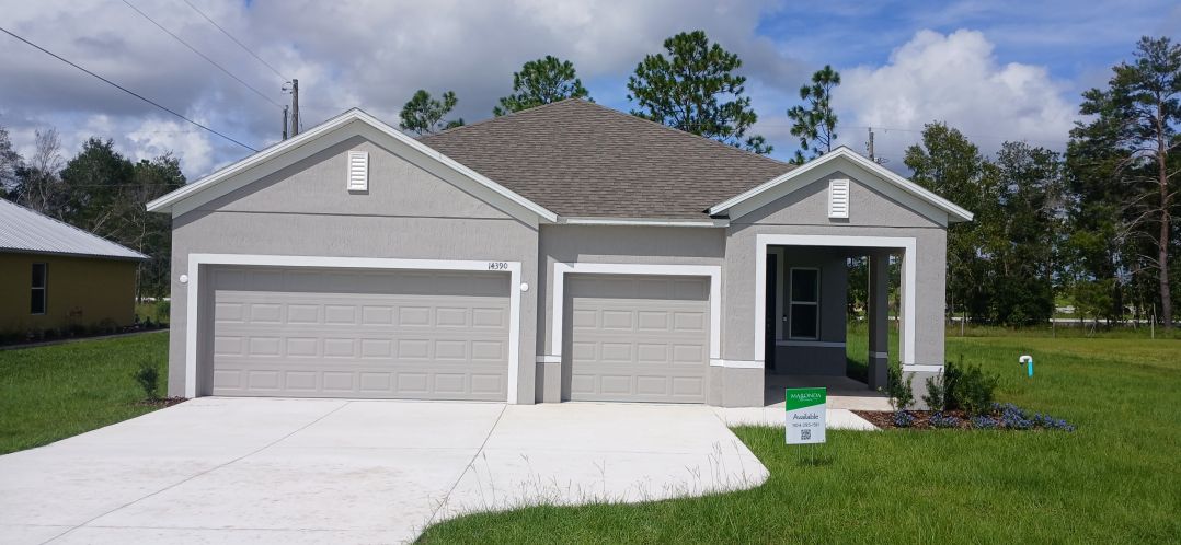A modern gray house with two garage doors, situated on a green lawn under a cloudy sky.