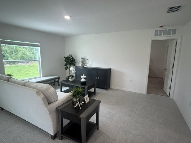 Bright living room with a beige sofa, black coffee table, and a decorative plant, featuring large windows and tile flooring.
