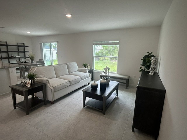A modern living room featuring a white sofa, dark coffee table, and plants on a light-colored tile floor.