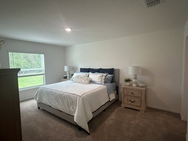 Bedroom featuring a bed with blue and white bedding, two bedside lamps, and a window with greenery outside.