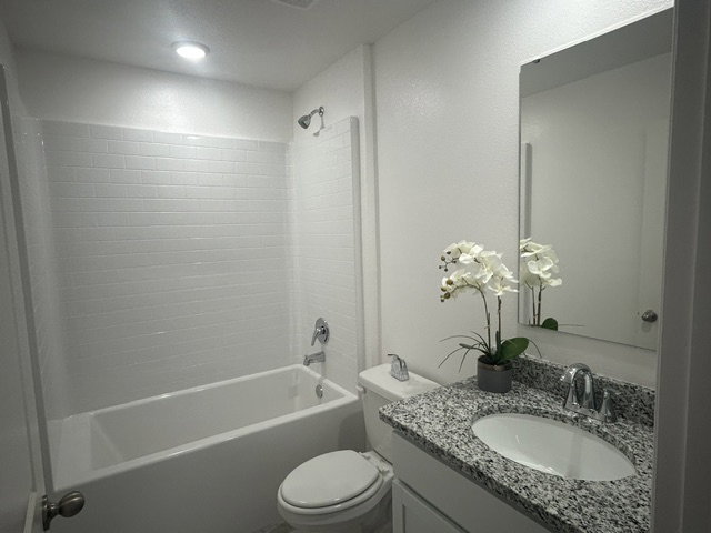 A clean, modern bathroom featuring a bathtub, white tiles, a vanity with a granite countertop, and a potted orchid.