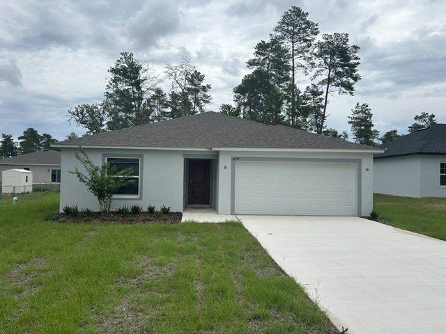 Single-story house with a gray roof and a white exterior, surrounded by green grass and trees.