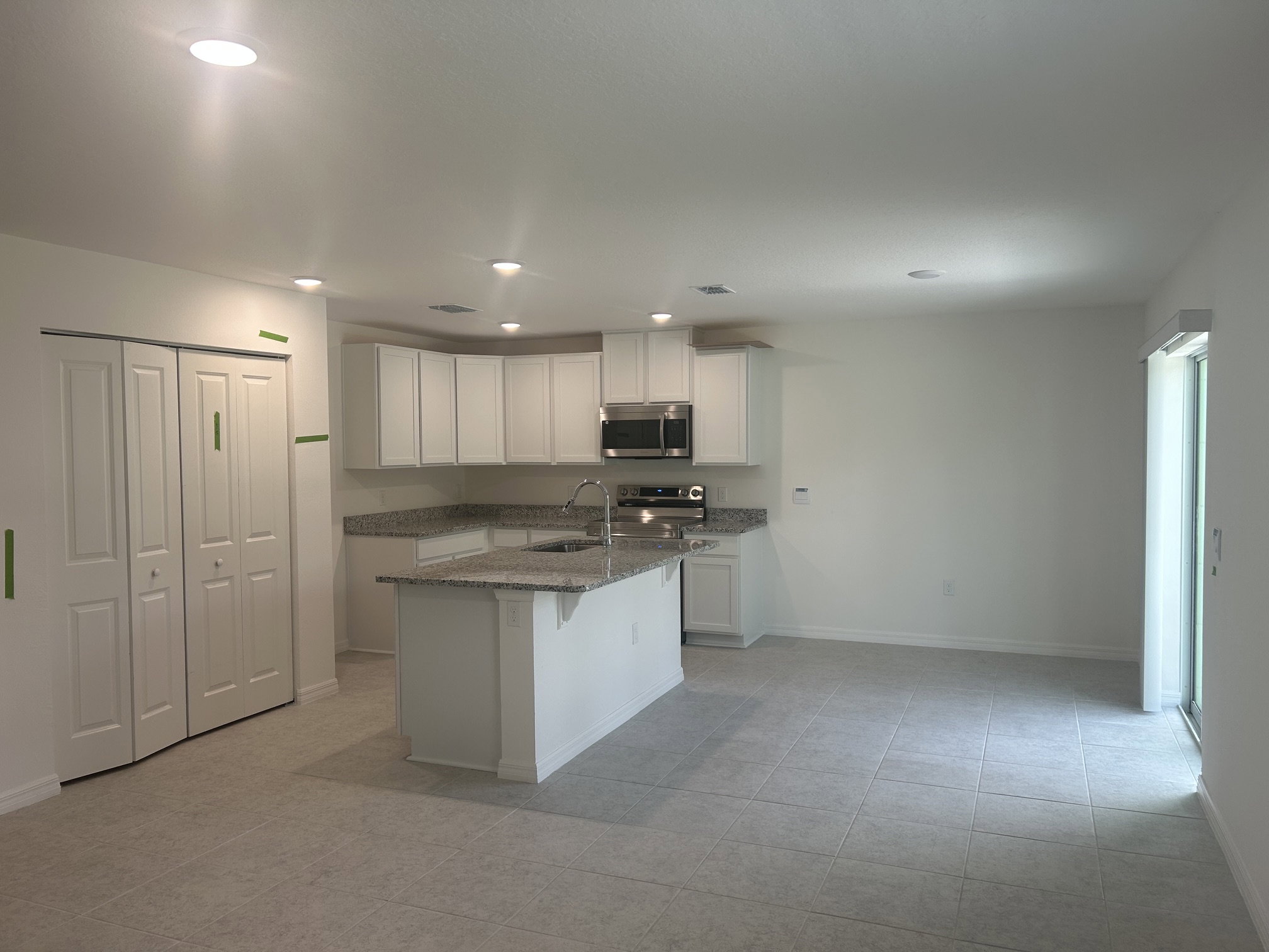 Modern kitchen with white cabinets, granite countertops, and stainless steel appliances, featuring an open layout and tile flooring.