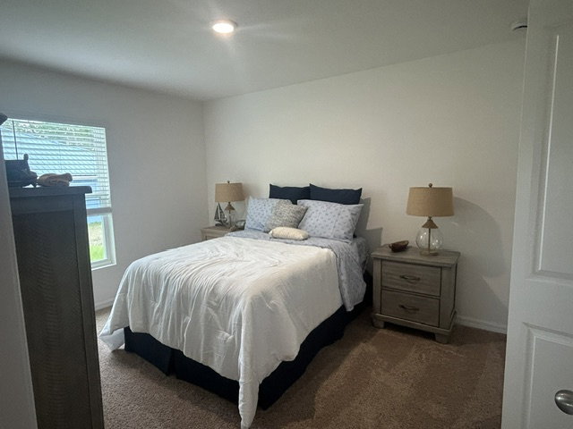 Cozy bedroom featuring a queen-sized bed with blue and white bedding, two bedside lamps, and a window with blinds.