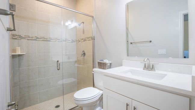Bright modern bathroom featuring a walk-in shower, a white sink with a countertop, and a toilet.