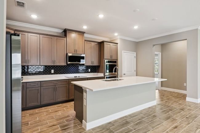 Modern kitchen featuring dark wood cabinetry, stainless steel appliances, and a central island with a white countertop.