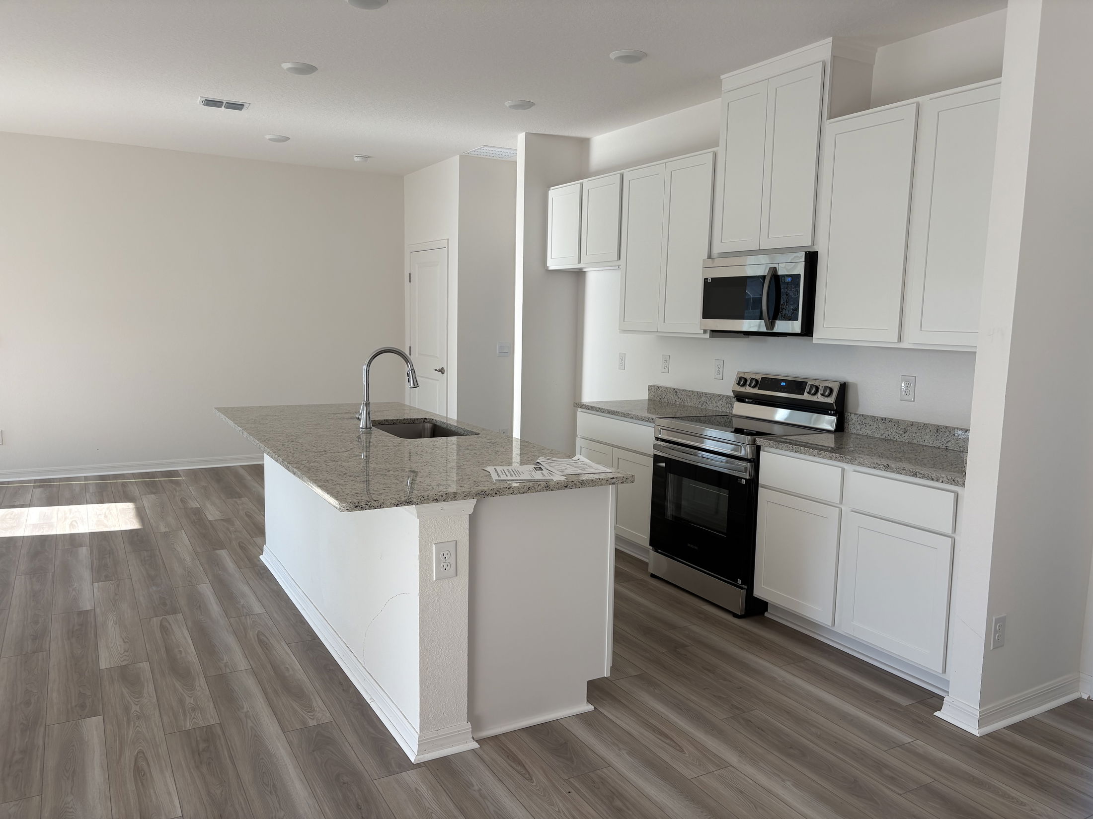 Modern kitchen with white cabinets, granite countertops, and stainless steel appliances featuring a wood laminate floor.