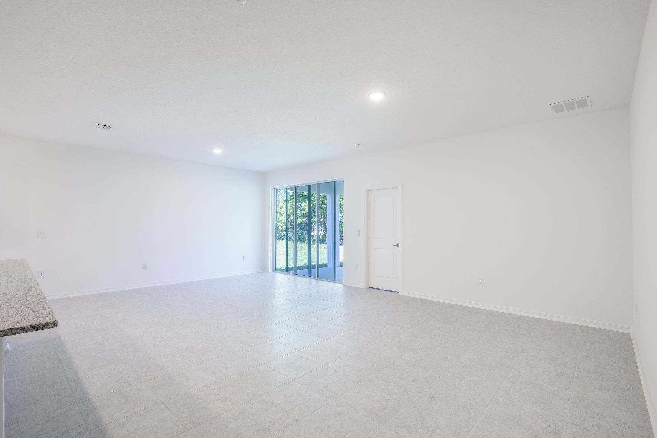 Spacious, empty living room with tiled floors, large sliding glass doors, and natural light.