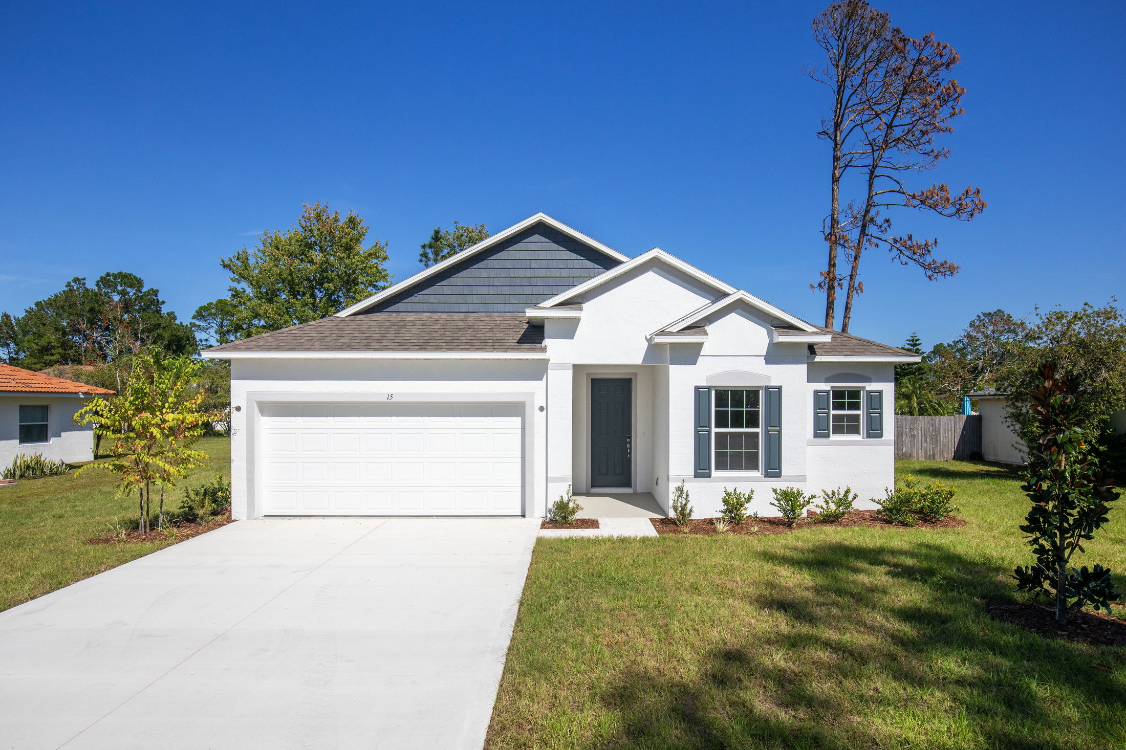 A modern, single-story white house with a two-car garage and well-maintained lawn under a clear blue sky.