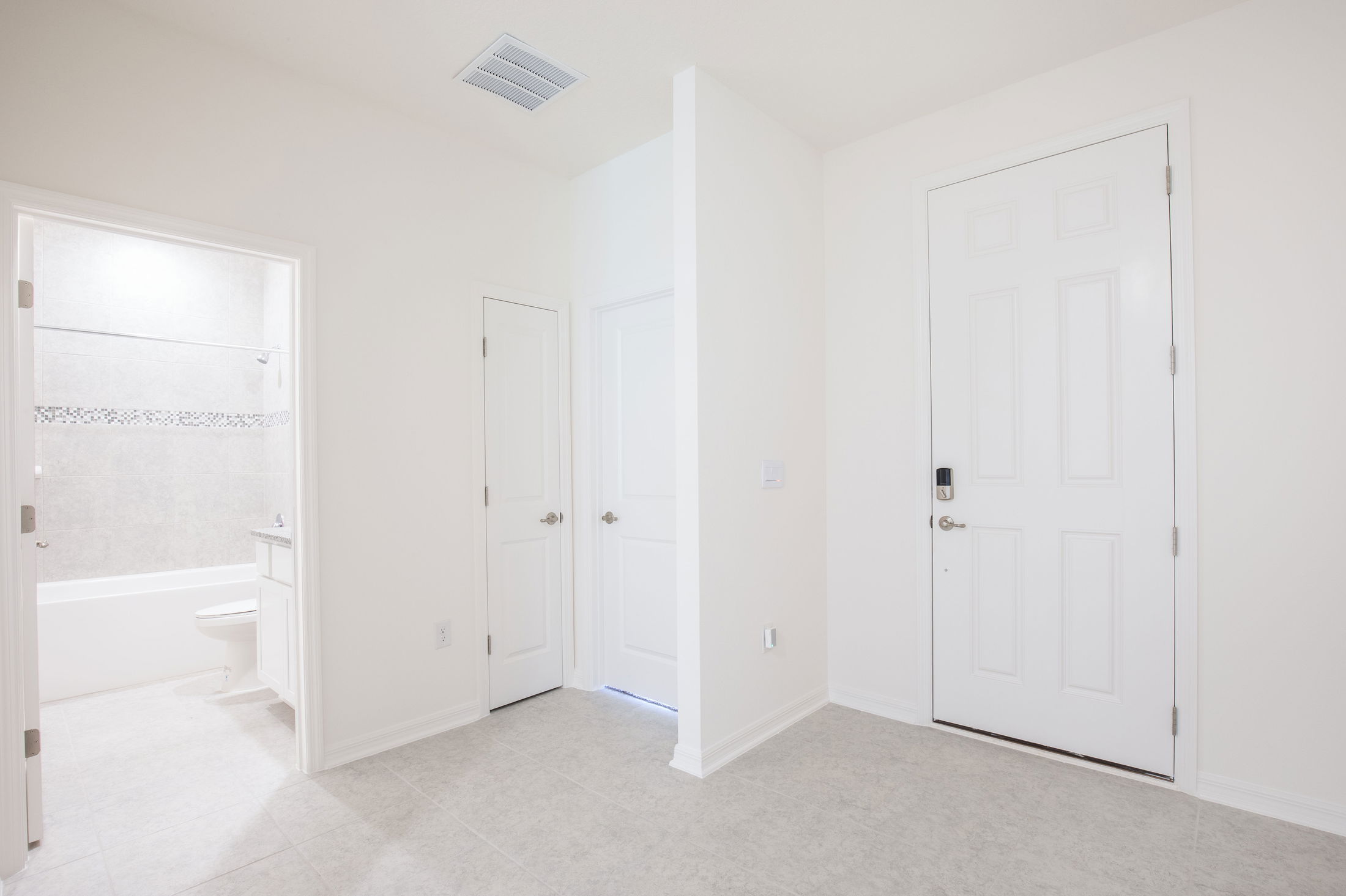 Minimalist white hallway with three closed doors and a view into a bright bathroom featuring a bathtub and tiled walls.