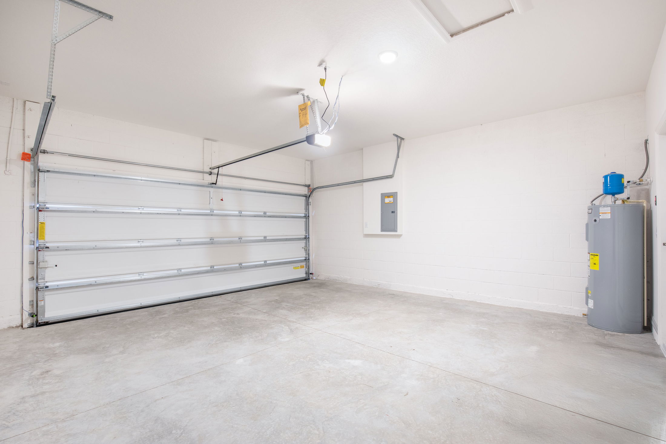 Empty residential garage with a concrete floor, closed garage door, water heater, and electrical panel on the wall.