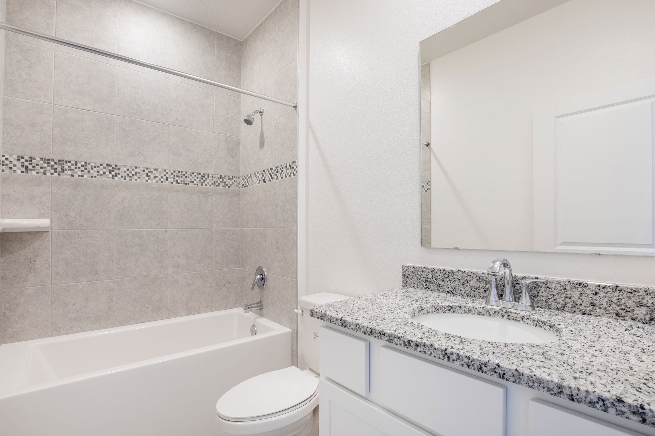 Modern bathroom with granite countertop, white cabinets, and a tiled shower and bathtub combination.