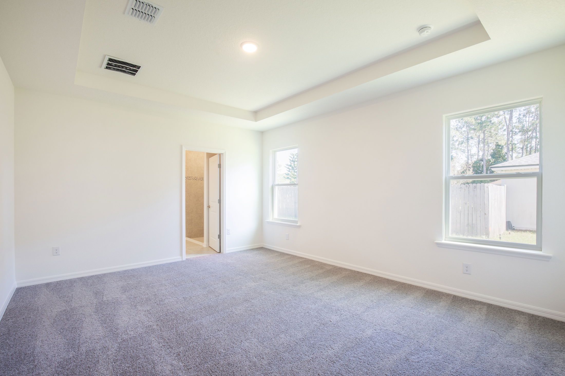 Spacious empty bedroom with carpet flooring, two windows, and an open door leading to a bathroom.