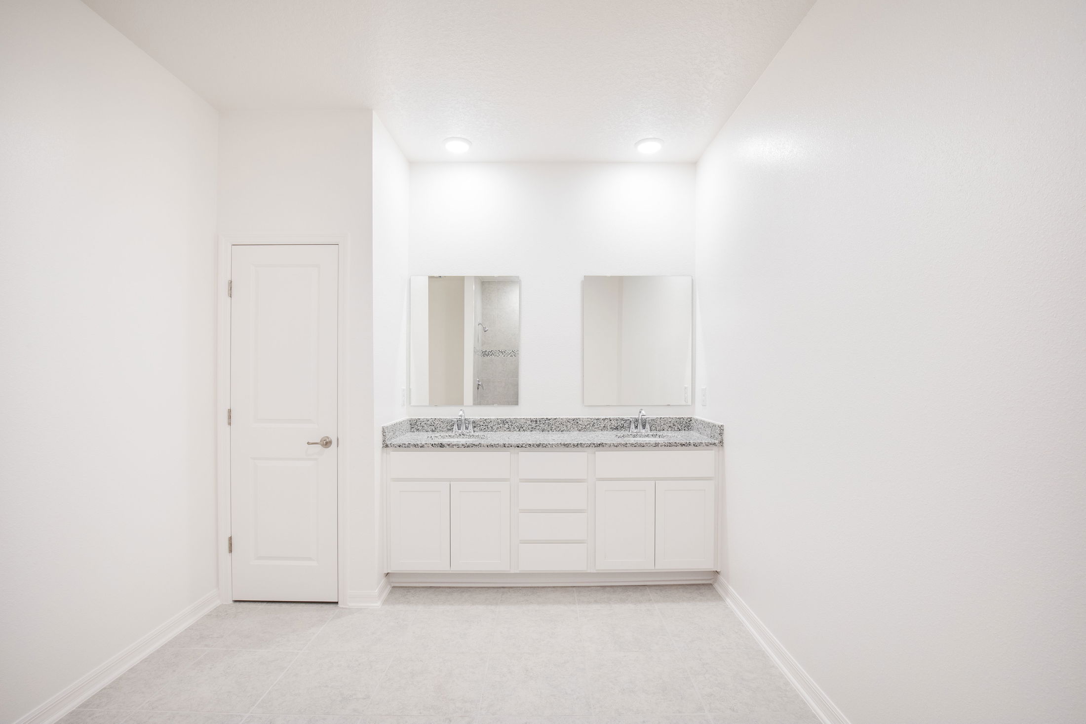Modern white bathroom with a double sink vanity and granite countertop, featuring two mirrors and recessed lighting.