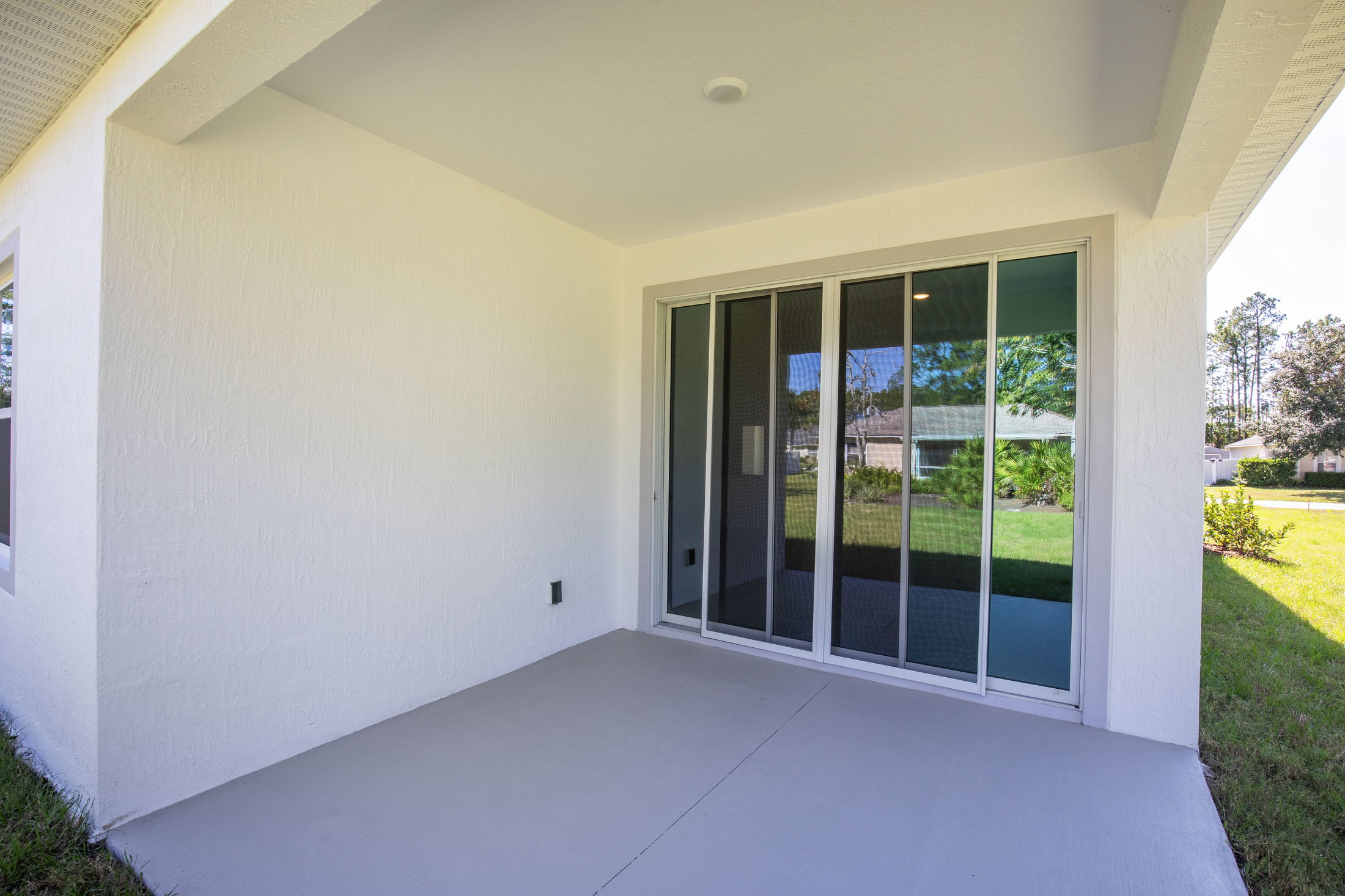 Covered patio with sliding glass doors and a view of a grassy backyard.
