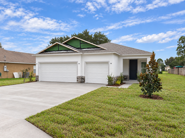 A modern single-family home with a two-car garage, manicured lawn, and blue sky.